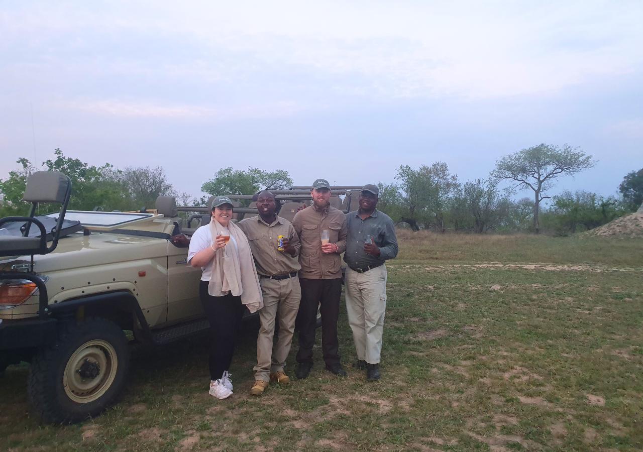 Four people standing in front of a safari vehicle holding drinks