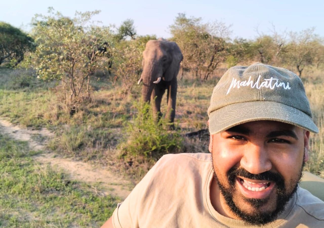 man taking a selfie on safari with an elephant in the background