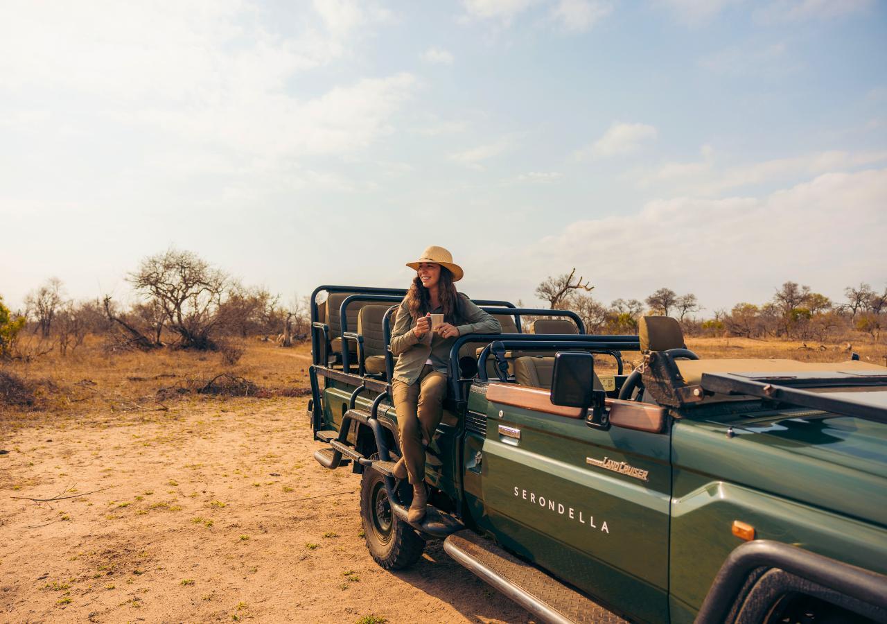 woman standing on the side of a safari vehicle holding a mug (Copyright Mahlatini)