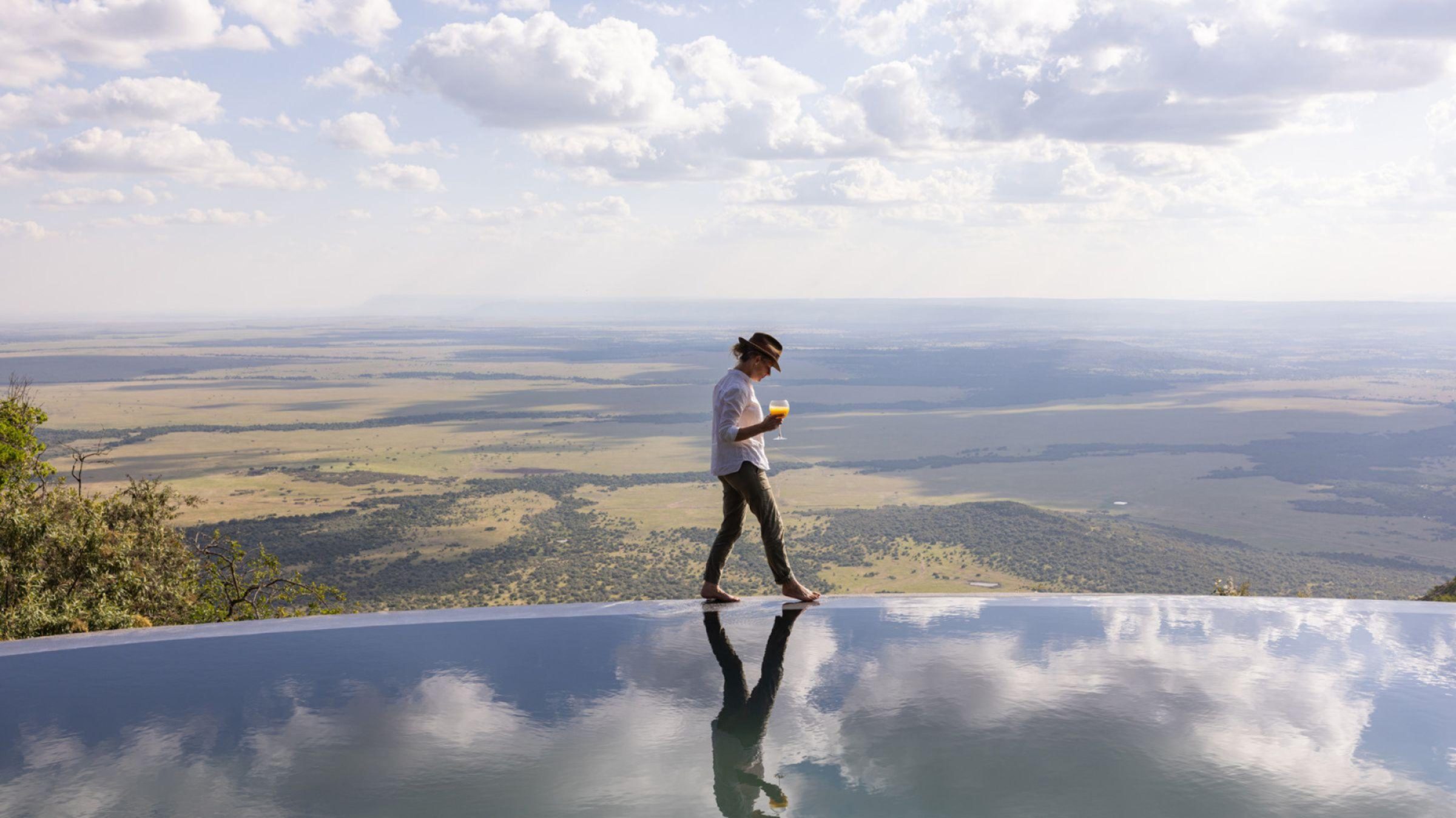 Wild Hill Hero image of woman walking around rim of pool with view of maasai mara in background