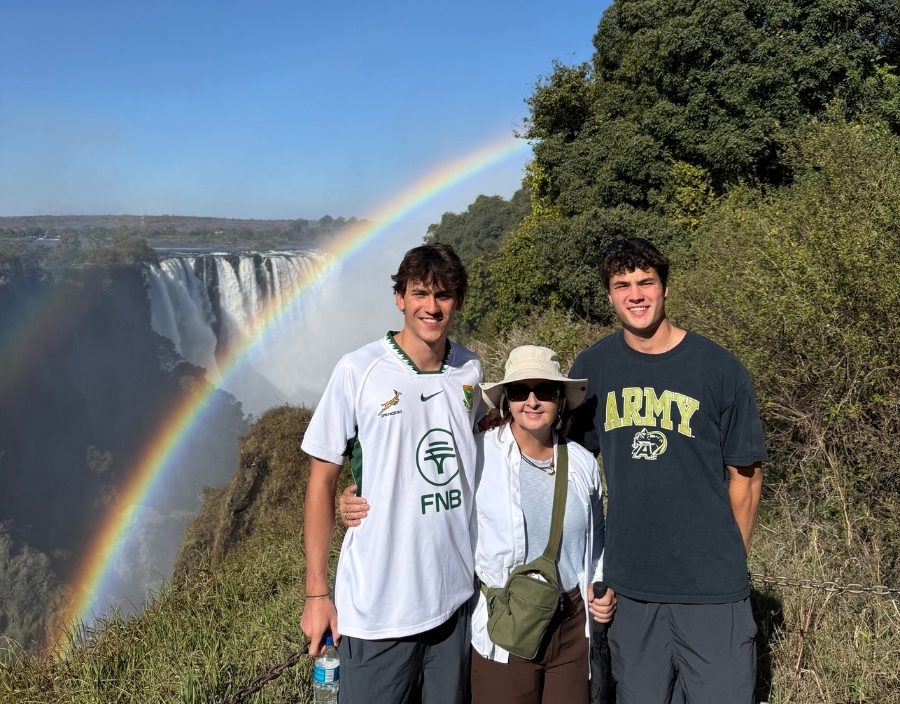 Woman and two men pose in front of rainbow at victoria falls