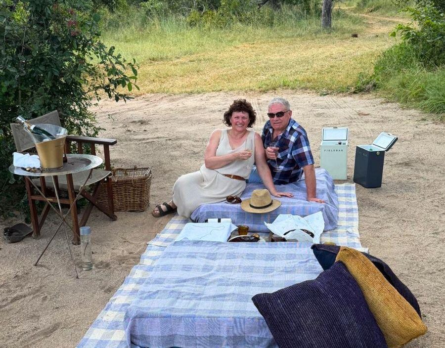 Couple pose on picnic blanket on safari in Zimbabwe