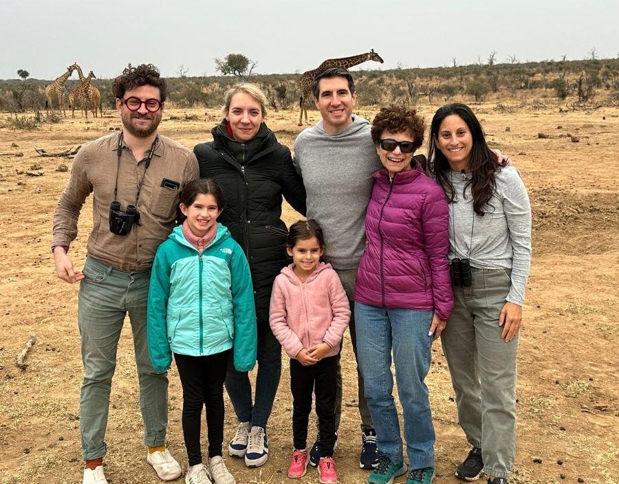 Family pose for photo in South African bush with giraffe in background