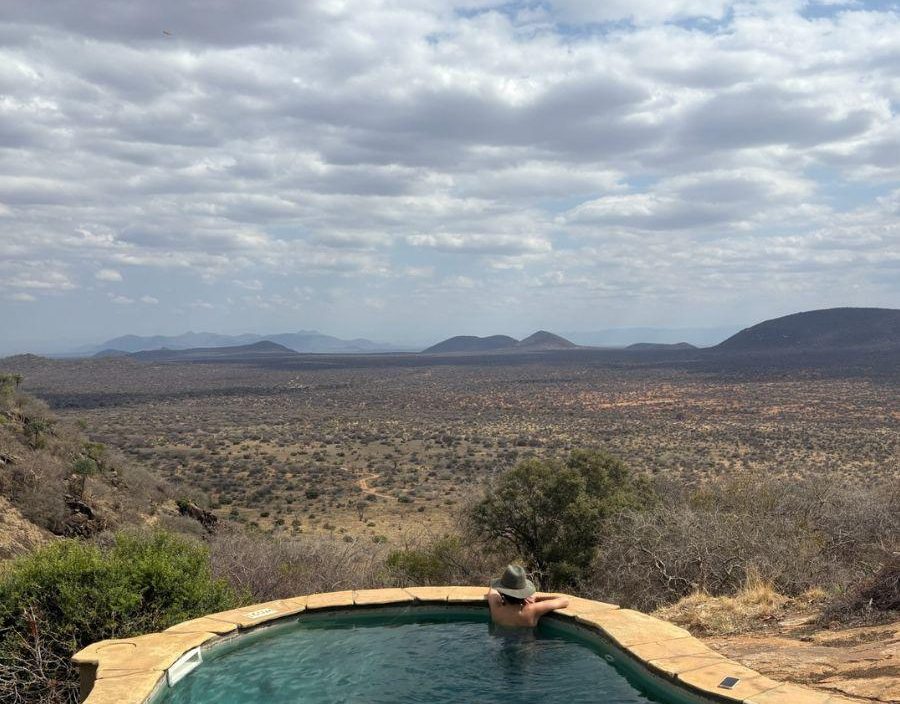 Woman looks out at African bushveld from a lodge pool in Kenya